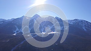 Aerial view of ski resort during a vibrant winter day. Clip. Flying over the snowy forested mountains on blue clear sky