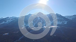 Aerial view of ski resort during a vibrant winter day. Clip. Flying over the snowy forested mountains on blue clear sky