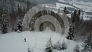 Aerial view of a skier on a mountain covered with pine trees. Skier waves hands and starts moving. Birds Eye View Above