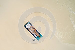 Aerial view of slim woman sunbathing lying on a beach chair in Maldives. Summer seascape with girl, beautiful waves, colorful