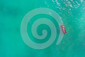 Aerial view of slim woman swimming on the swim mattress in the transparent turquoise sea. Summer seascape with girl, beautiful