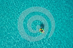 Aerial view of slim woman swimming on the swim ring donut in the transparent turquoise sea in Seychelles. Summer seascape with