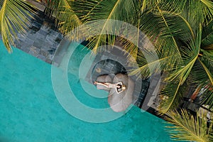 Aerial view of slim young woman in beige bikini and straw hat relaxing near luxury swimming pool and palm trees.Vacation