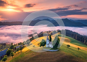 Aerial view of small church on the hill over pink low clouds