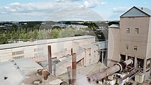 Aerial view of a small factory with smoking chmneys. Stock footage. Flying above the factory surrounded by green trees