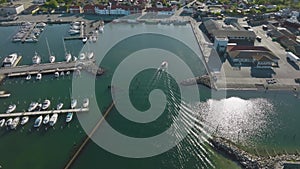 An aerial view of a small fishing port with industrial buildings, warehouses, and yachts. A small fishing ship is sailing in the p