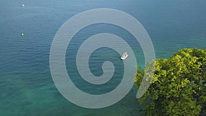 Aerial view of small motor boat floating in the turquoise sea water near the large green tree. Action. Summer resort