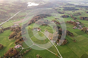 Aerial view of small scattered farm houses with red tiled roofs among green farming fields and distant forest in summer