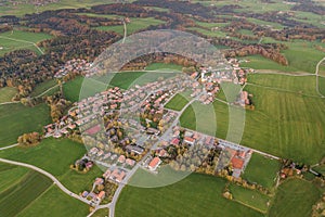 Aerial view of small town with red tiled roofs among green farm fields and distant forest in summer