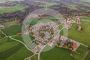 Aerial view of small town with red tiled roofs among green farm fields and distant forest in summer