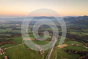 Aerial view of small town with red tiled roofs among green farm fields and distant forest in summer