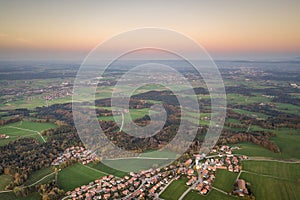 Aerial view of small town with red tiled roofs among green farm fields and distant forest in summer