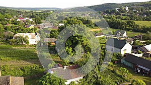 Aerial view of small village with small houses among green trees with farm fields and distant forest in summer.