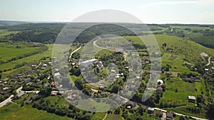 Aerial view of small village with small houses among green trees with farm fields and distant forest in summer.