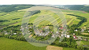 Aerial view of small village with small houses among green trees with farm fields and distant forest in summer.