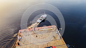 Aerial view of small wooden ferry crossing the river with orange car on it. Traditional ferry boat on water