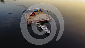 Aerial view of small wooden ferry crossing the river with orange car on it. Traditional ferry boat on water