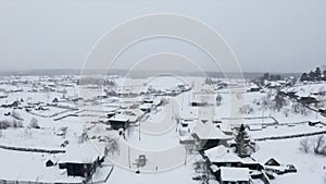 Aerial view of snow covered roofs of wooden houses. Clip. Small winter village on a heavy cloudy sky background.