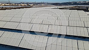 Aerial view of snow covered sustainable electric power plant with many rows of solar photovoltaic panels for producing