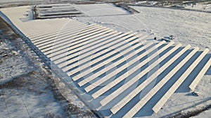 Aerial view of snow covered sustainable electric power plant with many rows of solar photovoltaic panels for producing