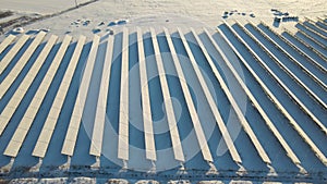 Aerial view of snow covered sustainable electric power plant with many rows of solar photovoltaic panels for producing