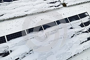 Aerial view of snow covered sustainable electric power plant with rows of solar photovoltaic panels for producing clean