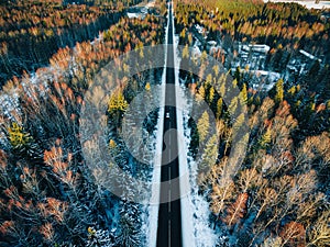 Aerial view of snow covered trees in forest and winter country road with a car