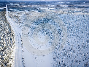 Aerial view of snow covered winter forest and road. Beautiful rural landscape in Finland