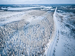 Aerial view of snow covered winter forest and road. Beautiful rural landscape in Finland