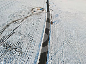 Aerial view of snow fields splitted by tar road with lines of offroad car in field