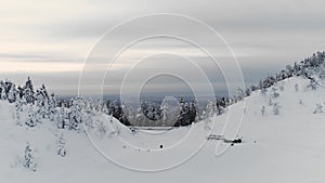 aerial view of snow mountain land. Dark Pine forest and city in background. Cloudy sky in a winter journey