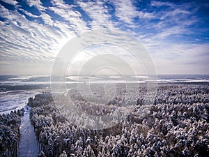 Aerial view on snow winter forest and field near road. Frozen river on background. Clouds with sun in blue sky