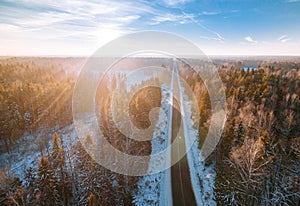 Aerial view of snow winter road in the forest with morning sun