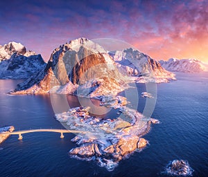 Aerial view of snowy island with rorbu, sea, bridge, rocks