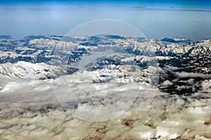Aerial view of snowy mountains in winter. Flying above the clouds