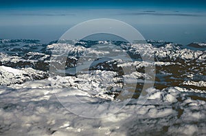 Aerial view of snowy mountains in winter. Flying at sunset above the clouds