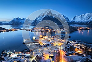 Aerial view of snowy village, city lights, sea, mountain at night