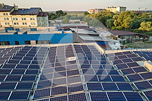 Aerial view of solar power plant with blue photovoltaic panels mounted on industrial building roof for producing green