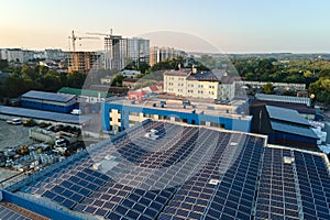 Aerial view of solar power plant with blue photovoltaic panels mounted on industrial building roof for producing green