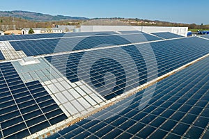 Aerial view of solar power plant with blue photovoltaic panels mounted on industrial building roof for producing green