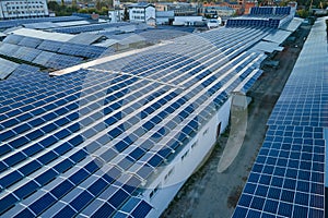 Aerial view of solar power plant with blue photovoltaic panels mounted on industrial building roof for producing green