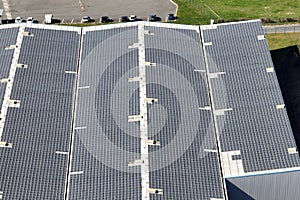 Aerial view of solar power plant with blue photovoltaic panels mounted on industrial building roof for producing green