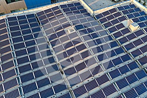 Aerial view of solar power plant with blue photovoltaic panels mounted on industrial building roof for producing green