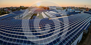 Aerial view of solar power plant with blue photovoltaic panels mounted on industrial building roof for producing green