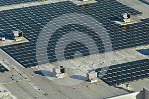 Aerial view of solar power plant with blue photovoltaic panels mounted on industrial building roof for producing green
