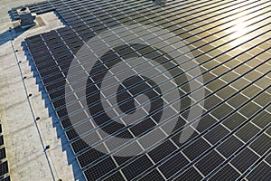 Aerial view of solar power plant with blue photovoltaic panels mounted on industrial building roof for producing green