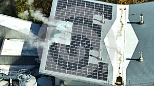 Aerial view of solar power plant with blue photovoltaic panels mounted on industrial building roof for producing green