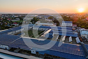 Aerial view of solar power plant with blue photovoltaic panels mounted on industrial building roof for producing green