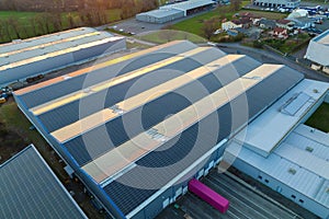 Aerial view of solar power plant with blue photovoltaic panels mounted on industrial building roof for producing green