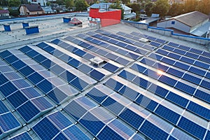 Aerial view of solar power plant with blue photovoltaic panels mounted on industrial building roof for producing green